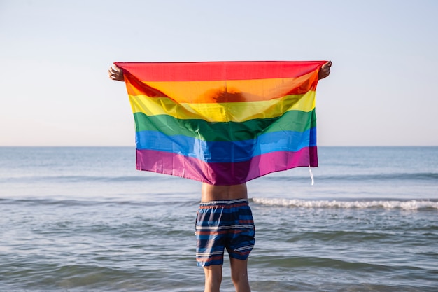 Jonge latino man die een lgtbi-vlag op het strand heft