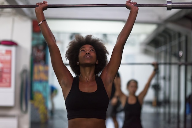 Foto jonge leuke afro-amerikaanse sportvrouw in de fitnessruimte die lege bar opheft