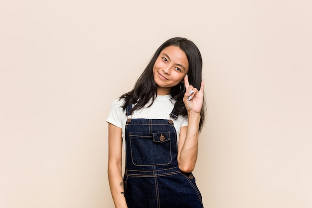 Jonge leuke chinese jonge blonde vrouw die een jas draagt tegen een roze muur die een hoornsgebaar toont als revolutieconcept.