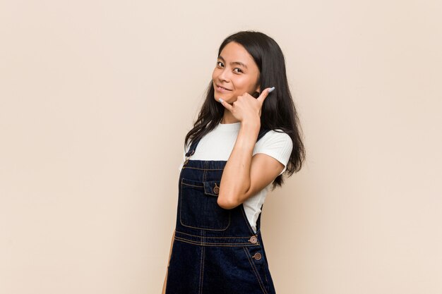 Jonge leuke Chinese tiener tegen een roze muur die een mobiel telefoongesprekgebaar met vingers toont.