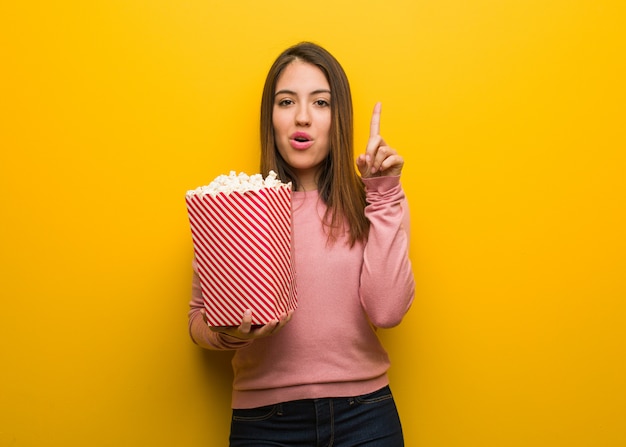 Jonge leuke vrouw die een popcornemmer houdt die een groot idee, concept creativiteit heeft