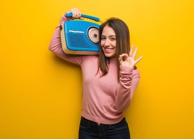 Jonge leuke vrouw die een uitstekende radio houdt die vrolijk en zeker ok gebaar doet