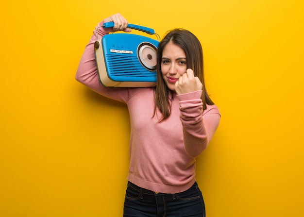 Jonge leuke vrouw die een uitstekende radio houdt die vuist toont aan voorzijde, boze uitdrukking