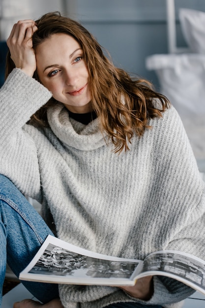 Jonge leuke vrouw in een gezellige trui die in bed zit en een boek vasthoudt