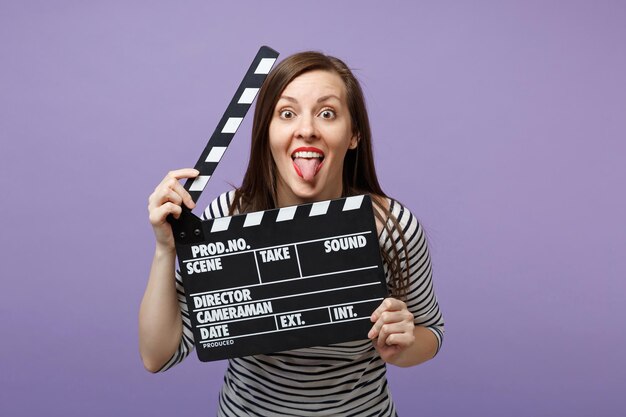 Jonge leuke vrouw meisje in casual gestreepte kleding poseren geïsoleerd op violet paarse achtergrond studio portret. Mensen oprechte emoties levensstijl concept. Bespotten kopie ruimte. Filmklapper vasthouden