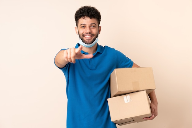 Jonge levering Marokkaanse man geïsoleerd op beige muur wijst vinger naar je met een zelfverzekerde uitdrukking