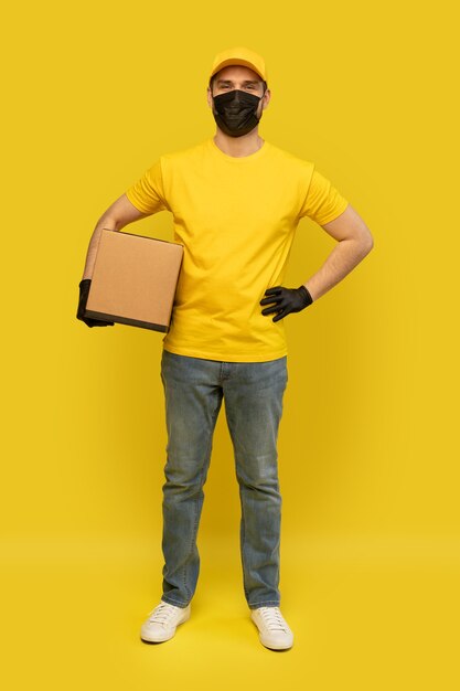 Jonge leveringsmens in gele t-shirt, masker, handschoenen met geïsoleerde doos