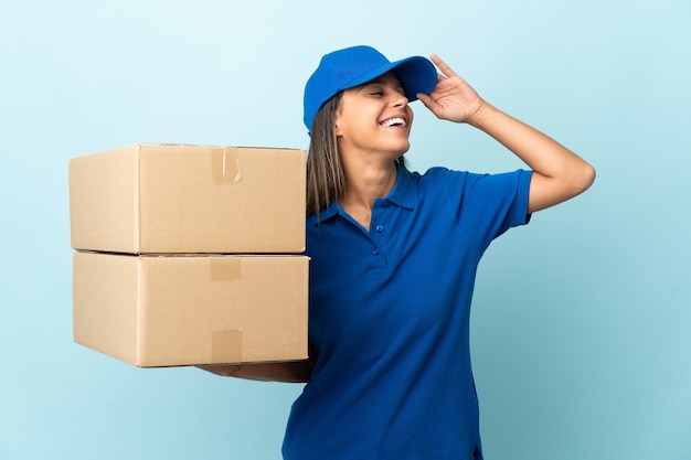 Jonge leveringsvrouw die op blauw wordt geïsoleerd dat veel glimlacht