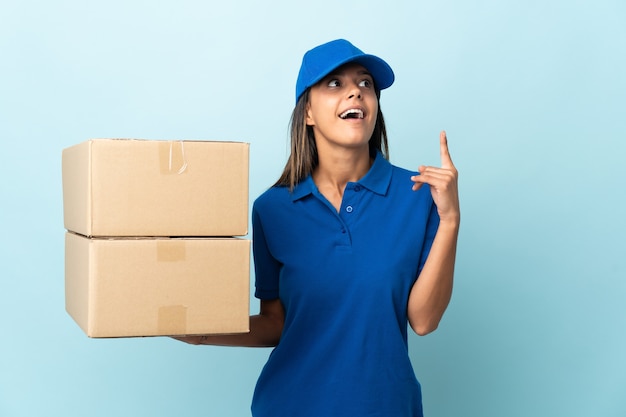 Jonge leveringsvrouw die op blauwe achtergrond wordt geïsoleerdd die een idee denken dat de vinger benadrukt