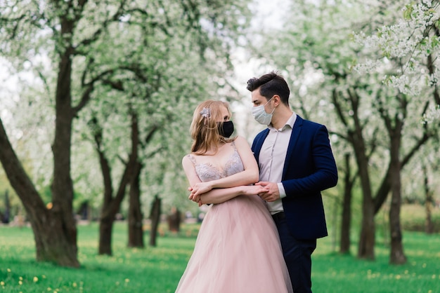 Jonge liefdevolle bruiden in park met medische maskers tijdens quarantaine op hun trouwdag