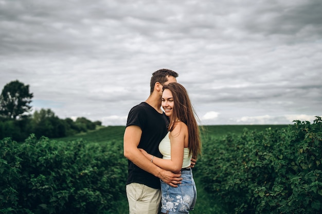 Jonge liefdevolle paar zachtjes knuffelen op groene bes plantages. Liefdesverhaal