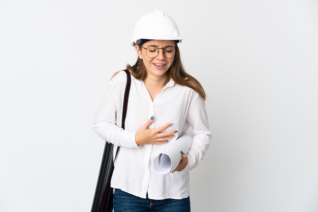 Jonge Litouwse architectenvrouw met helm en blauwdrukken die op witte achtergrond worden geïsoleerd die veel glimlachen