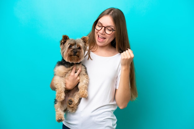 Jonge Litouwse vrouw die een hond houdt die op blauwe achtergrond wordt geïsoleerd en een overwinning viert