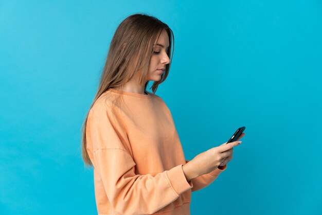 Jonge Litouwse vrouw die op blauwe muur wordt geïsoleerd die een bericht of e-mail met mobiel verzendt