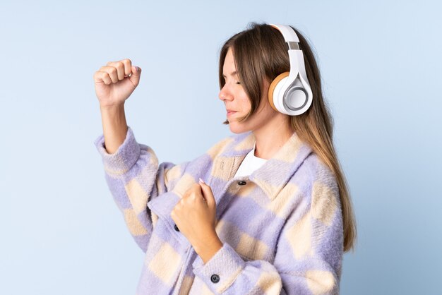 Jonge Litouwse vrouw geïsoleerd op blauwe achtergrond muziek luisteren en dansen