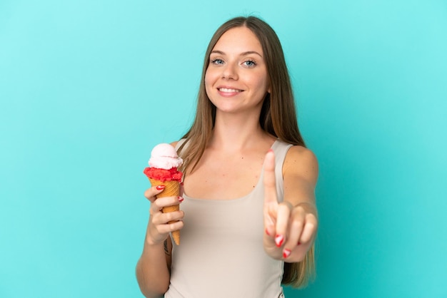Jonge Litouwse vrouw met cornet-ijs geïsoleerd op een blauwe achtergrond die een vinger laat zien en optilt