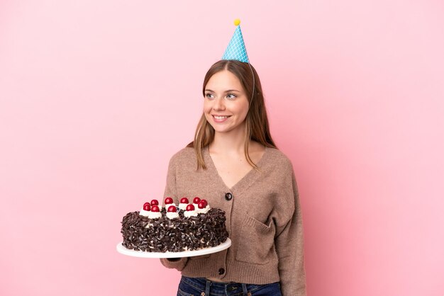 Jonge Litouwse vrouw met verjaardagstaart geïsoleerd op roze achtergrond op zoek naar kant