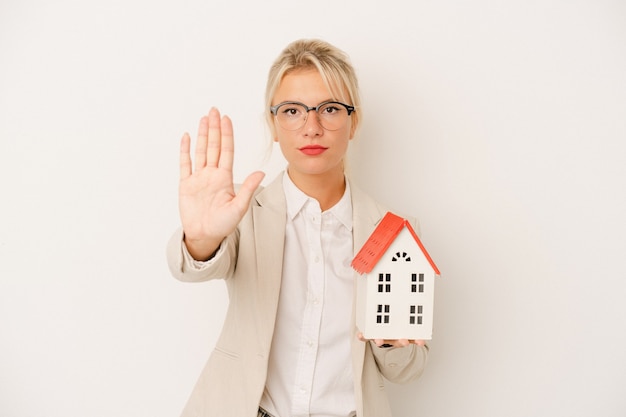 Jonge makelaar vrouw met een huis model geïsoleerd op een witte achtergrond permanent met uitgestrekte hand weergegeven: stopbord, voorkomen dat u.