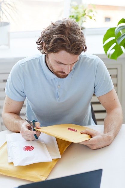 Jonge man aan de tafel zitten en de enveloppen thuis openen