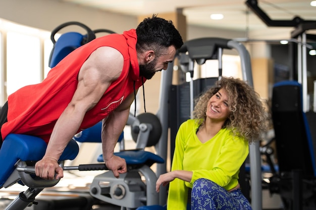 Jonge man aan het trainen in de sportschool doet rugoefening op de machine met hulp van haar trainer