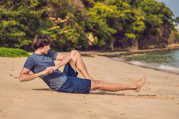 Jonge man aan het trainen op het strand, sportieve man die oefeningen doet