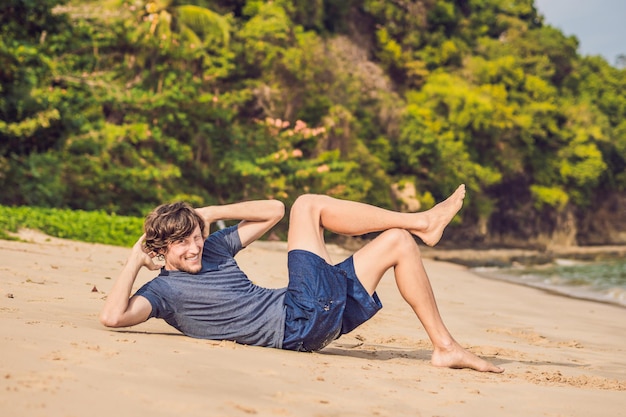 Jonge man aan het trainen op het strand, sportieve man die oefeningen doet