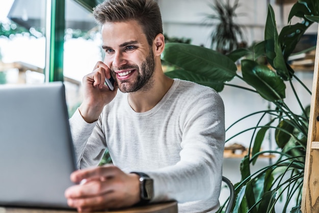 Jonge man aan het werk in de coffeeshop met behulp van mobiele telefoon en laptop