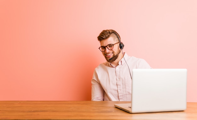 Jonge man aan het werk in een callcenter kijkt opzij lachend, vrolijk en aangenaam.