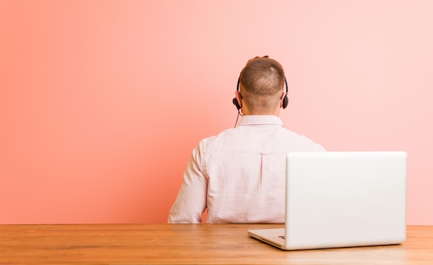 Jonge man aan het werk in een callcenter van achteren, terugkijkend.