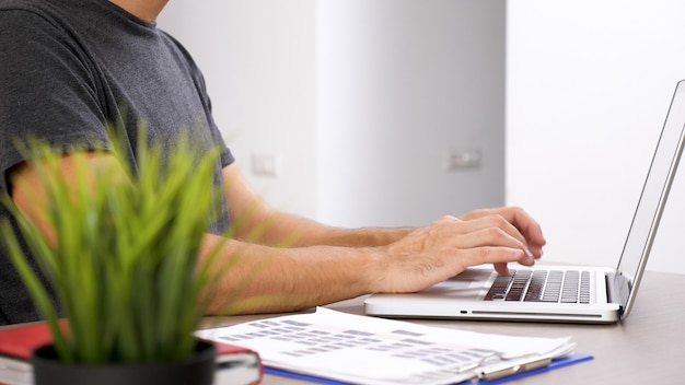 Jonge man aan het werk met laptop op zijn bedrijfsdocumentatie. Bedrijfspersoon op de werkplek.
