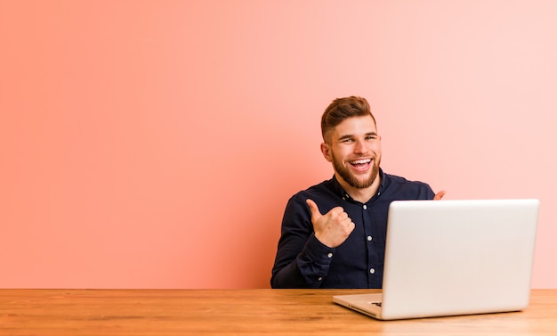 Jonge man aan het werk met zijn laptop beide duimen omhoog, glimlachen en zelfverzekerd.