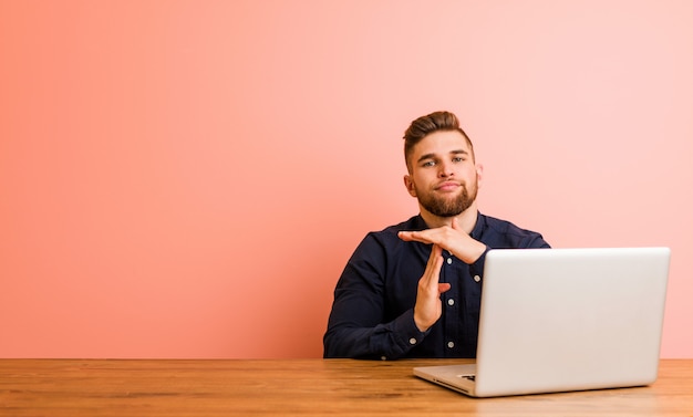 Jonge man aan het werk met zijn laptop met een time-out gebaar.