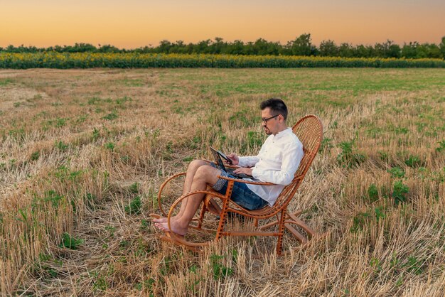 Jonge man aan het werk op afstand met netbook zittend in schommelstoel in weide tijdens zomervakantie