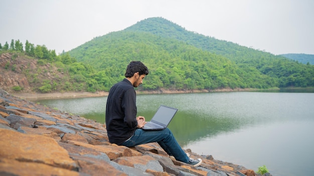 Jonge man aan het werk op een laptop en zittend in de natuur Workation en Digital Nomad concept