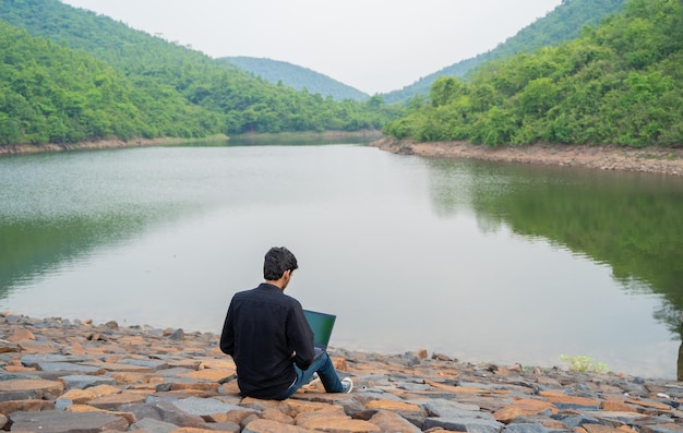 Jonge man aan het werk op een laptop en zittend in de natuur Workation en Digital Nomad concept