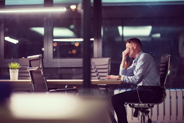 Jonge man aan het werk op laptop 's nachts in donkere kantoor. De ontwerper werkt in de latere tijd.