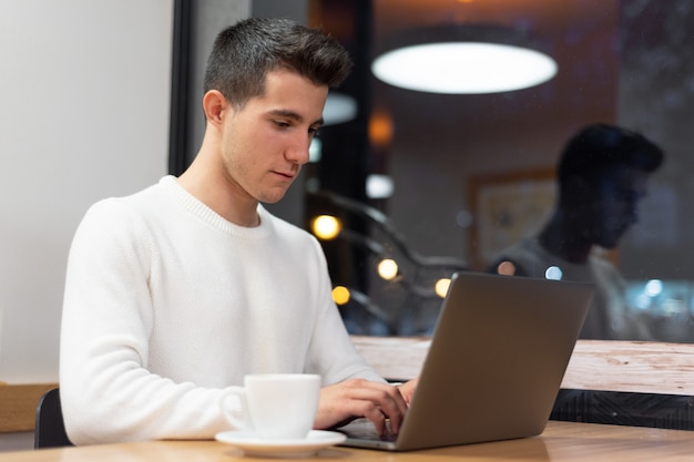 Jonge man aan het werk op zijn laptop in een koffieshop, jonge student te typen op de computer.