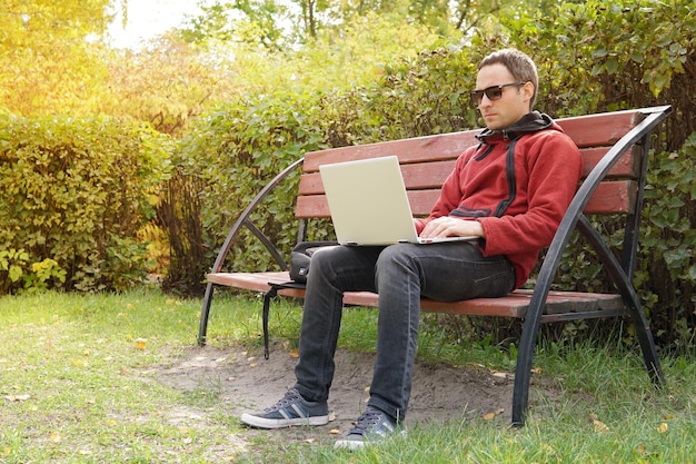 Jonge man aan het werk op zijn laptop verbinding maken met draadloos internet in landelijk gebied internet-verbinding stelt mensen in staat om overal te werken freelancer programmeur zittend op laptop op een bankje in het park buiten