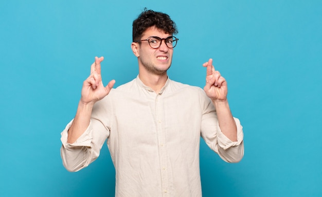 Jonge man angstig vingers kruisen en hopen op geluk met een bezorgde blik