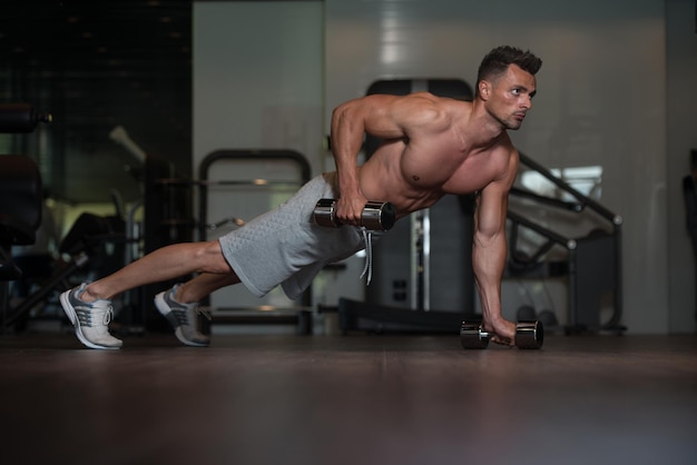 Jonge man atleet doet push-ups met halters als onderdeel van bodybuilding-training