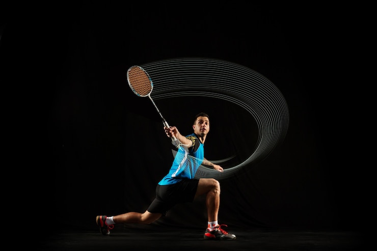 Foto jonge man badminton spelen over zwarte studio achtergrond. fit mannelijke atleet geïsoleerd op donker met led-lichtspoor. badmintonspeler in actie, beweging, beweging. aanvals- en verdedigingsconcept