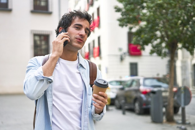 Jonge man beheerst de kunst van het multitasken met een afhaalkoffie in de hand en een productief telefoongesprek