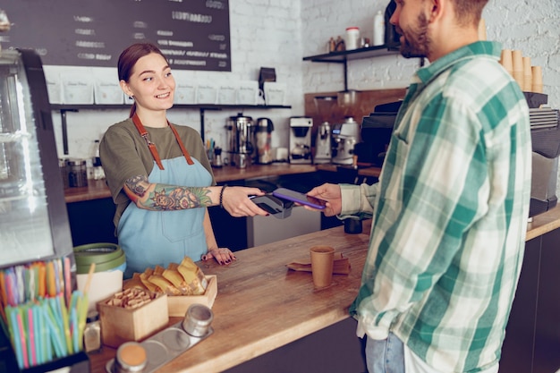 Jonge man betalen voor koffie met smartphone in café