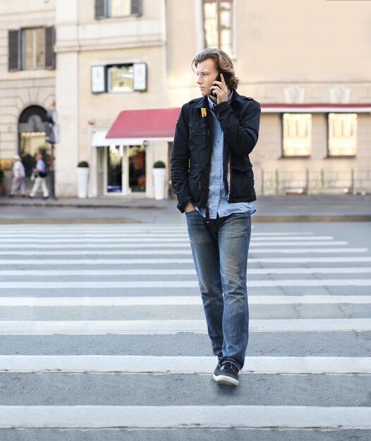 jonge man bij een voetgangersovergang op een stadsstraat met behulp van een smartphone