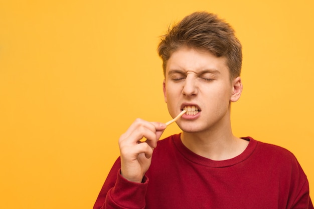 Jonge man bijt frietjes met gesloten ogen op een geel