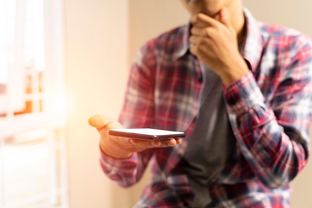 Jonge man brengt de tijd door met behulp van een mobiele smartphone, laat de kin op zijn hand rusten selectieve focus