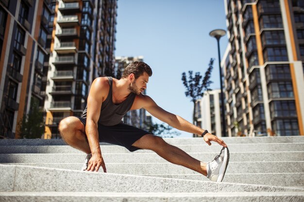 Jonge man buiten te oefenen. Foto van een sterke man die zijn been uitrekt en het met de hand vasthoudt. Alleen staan in yogapositie. Opwarmen voor de training of de training beëindigen met strekken.