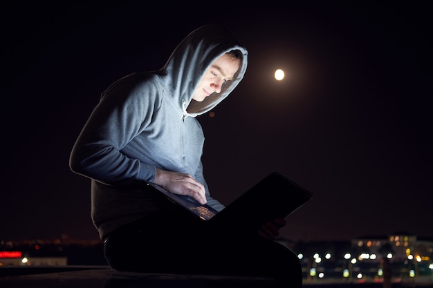 Jonge man buiten zitten en werken met laptop in de nacht,