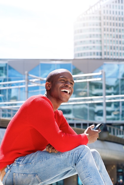 jonge man buiten zitten met mobiele telefoon en lachen