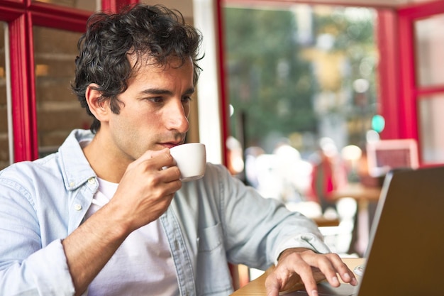 Jonge man concentreert zich op werk met laptop in gezellig café